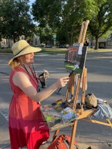 Artist in a red dress and hat painting outside